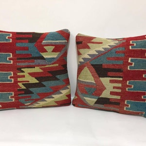 May include: Two decorative throw pillows with a geometric pattern in shades of red, blue, green, and brown. The pillows are made of woven fabric and have a traditional design.