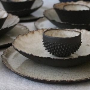 May include: A set of black and white ceramic plates and bowls with a textured, uneven edge. The bowl has a spiky, textured exterior.