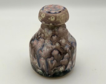 May include: A small ceramic jar with a lid, featuring a mottled glaze in shades of brown, pink, blue, and white.
