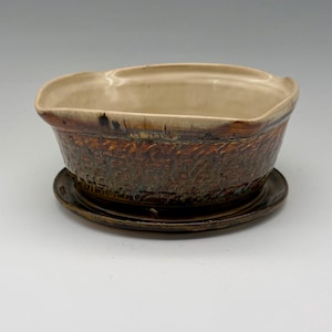 May include: A ceramic planter bowl with a textured, dark brown exterior featuring a relief pattern and a smooth, cream-colored interior. The bowl has an irregular, wavy rim and sits on a matching circular dark brown ceramic saucer base.
