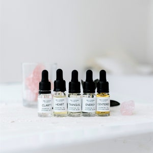 May include: Six small glass bottles with black dropper tops and white labels. The labels have the words "INK + OCEAN BOTANICALS" and the names of essential oil blends: "Clarity", "Heart", "Tranquil", "Energy", and "Centered".