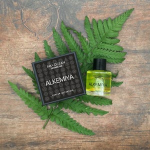 May include: A black box with the text "Ink + Ocean Botanicals Alkemiya Parfum Botanique" and a small bottle of yellow liquid with the same text.