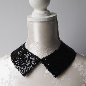 Puede incluir: Un collar negro de lentejuelas con forma puntiaguda y redondeada. El collar se muestra en un maniquí blanco.