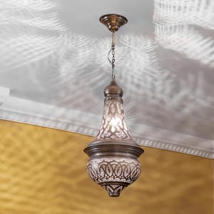 May include: An antique bronze-colored pendant light fixture with an intricate, openwork design. The light has a bulb inside, casting a warm glow and creating decorative shadows on the ceiling. The fixture is suspended from a chain.