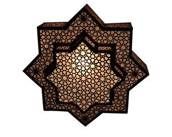 May include: A decorative, layered star-shaped lantern with intricate geometric cutouts. The lantern has a dark brown exterior and a warm, glowing interior. The design is reminiscent of Middle Eastern or Moroccan style.