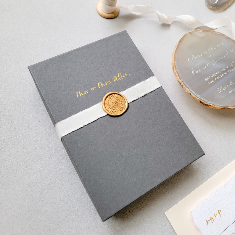 Personalized charcoal gray boxed wedding invitation, gold calligraphy by Jen, wrapped with a gold wax seal and cream hand-dyed silk ribbon, agate invitation and rsvp with envelope on a light gray background