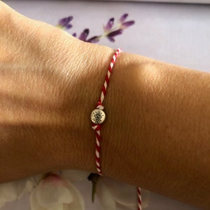May include: Red and white string bracelet with a silver charm featuring an eye symbol.