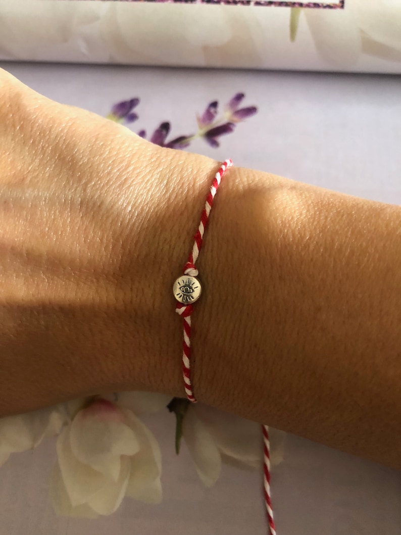 May include: Red and white string bracelet with a silver charm featuring an eye symbol.