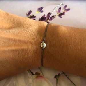 May include: A gray string bracelet with a silver charm featuring an eye symbol.