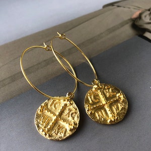 May include: Gold hoop earrings with a round pendant featuring a cross and the text "IC XC NIKA".