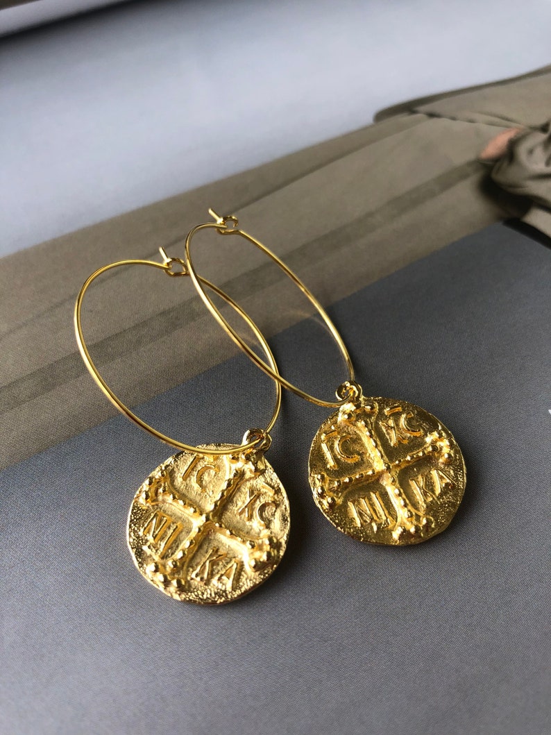 May include: Gold hoop earrings with a round pendant featuring a cross and the text "IC XC NIKA".