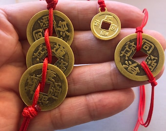 May include: A set of five gold-colored Chinese lucky coins strung together with red string. The coins have Chinese characters on them and a square hole in the center.