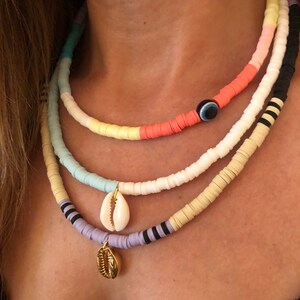 May include: A layered necklace with colorful beads and shell charms. The top layer features a blue evil eye charm. The necklace is made of white, light blue, yellow, pink, and black beads.