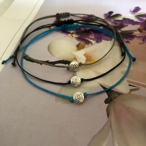 May include: Three layered bracelets with a silver charm featuring an eye symbol. The bracelets are gray, black, and blue.