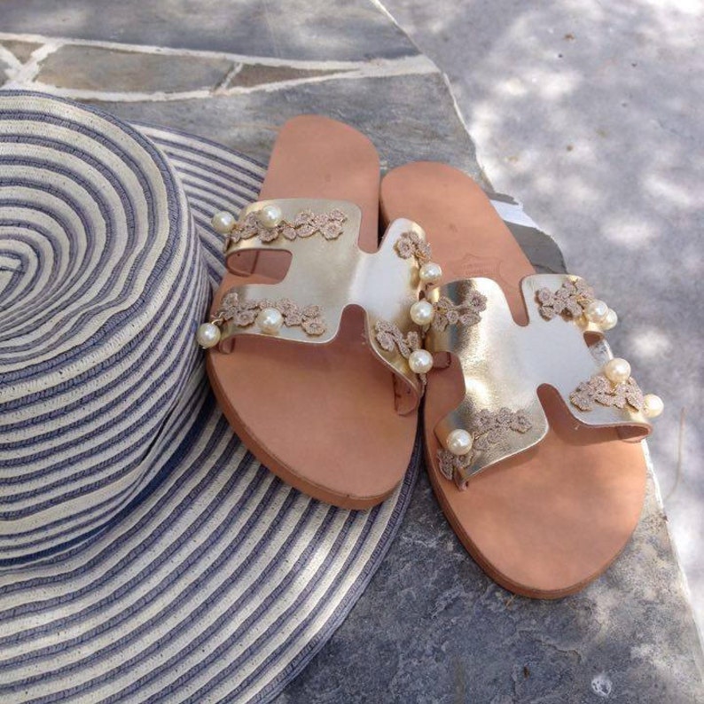 May include: A pair of gold leather sandals with delicate lace detailing and pearl accents. The sandals have a simple, strappy design and are perfect for summer.