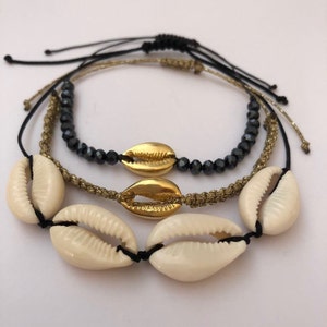 May include: Three layered bracelets with black beads, gold cowrie shells, and white cowrie shells.