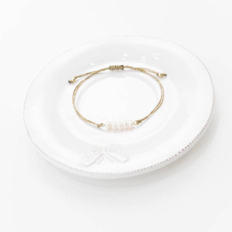 May include: A simple bracelet made with a gold cord and a row of white pearls.