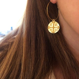 May include: Gold hoop earrings with a round pendant featuring a cross and the text "IC XC NIKA".