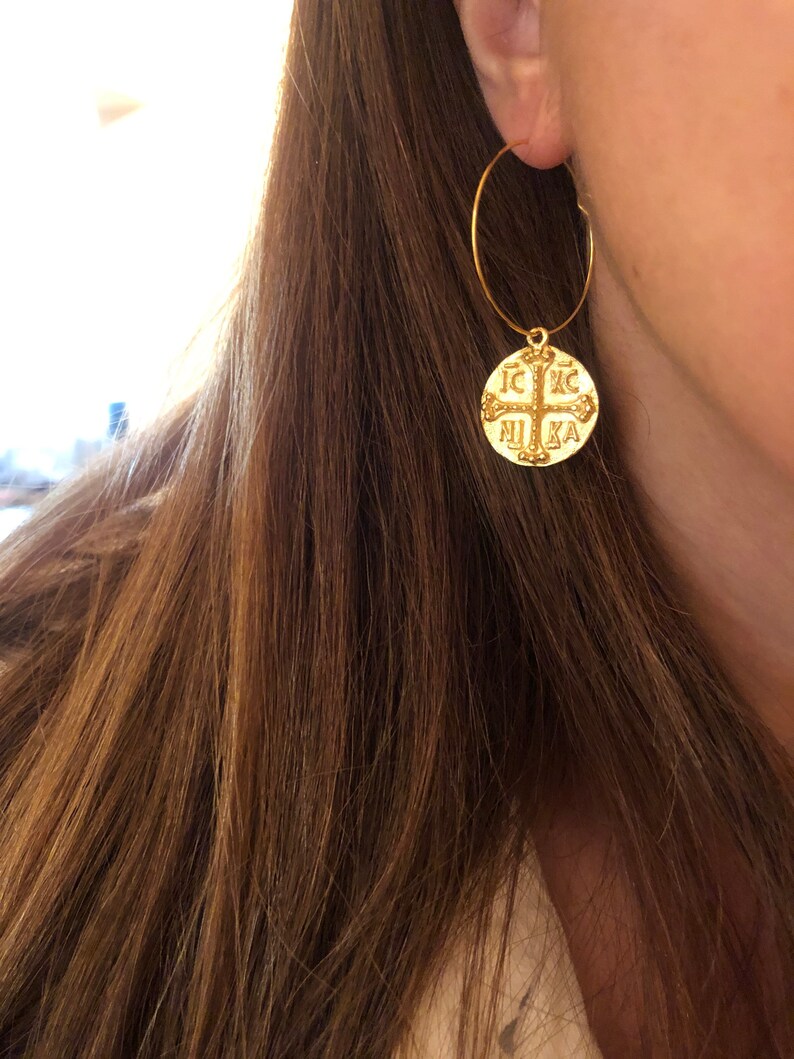 May include: Gold hoop earrings with a round pendant featuring a cross and the text "IC XC NIKA".