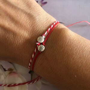 May include: Red and white string bracelet with two silver charms featuring an eye symbol.