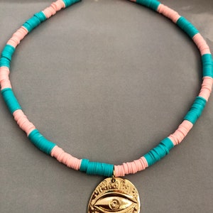 May include: A turquoise and pink beaded necklace with a gold evil eye pendant.