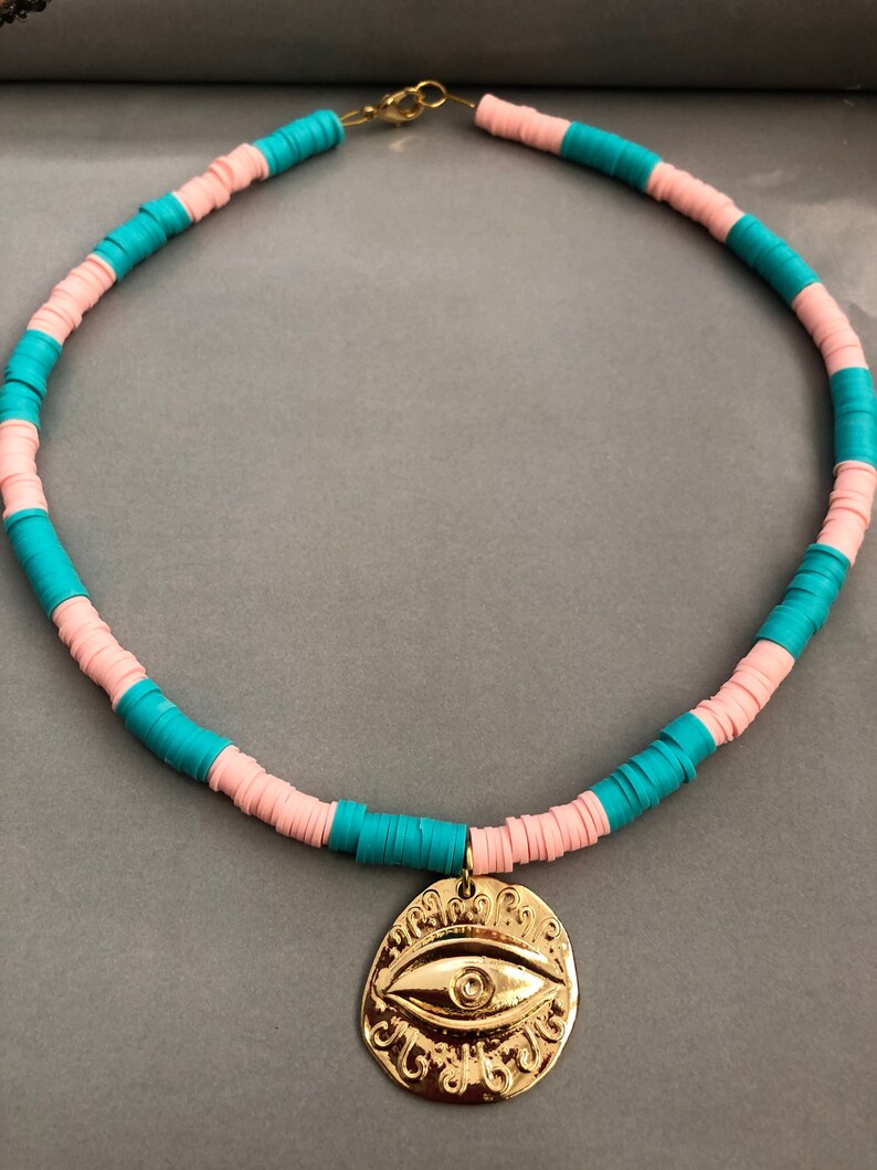 May include: A turquoise and pink beaded necklace with a gold evil eye pendant.