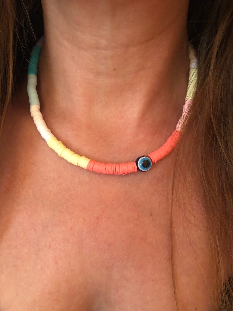May include: A colorful beaded necklace with a blue evil eye charm. The beads are in shades of light blue, yellow, and orange.