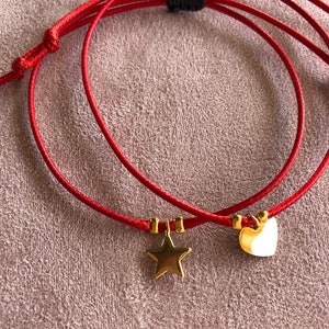 May include: Two red string bracelets with gold star and heart charms.