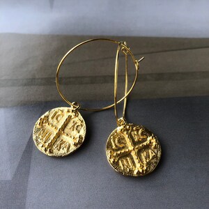May include: Gold hoop earrings with a coin-shaped pendant featuring a cross and the inscription "IC XC NIKA".