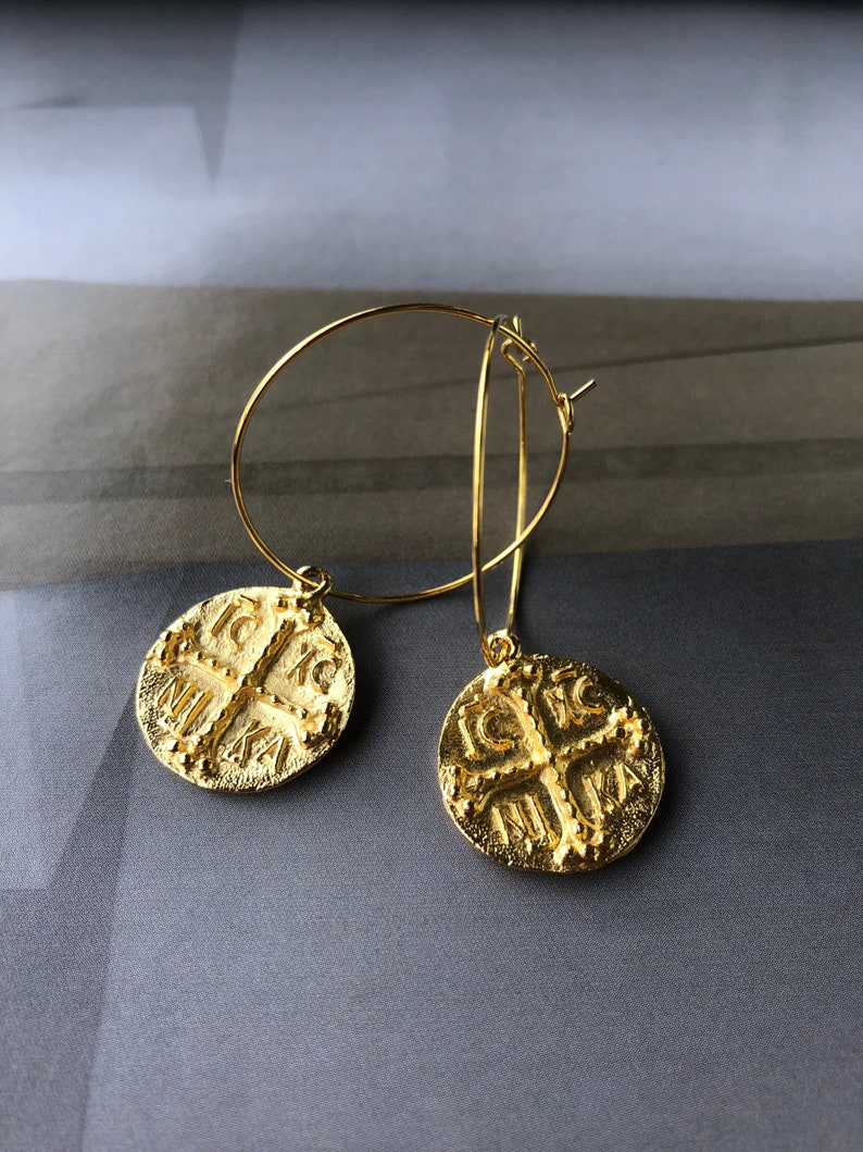 May include: Gold hoop earrings with a coin-shaped pendant featuring a cross and the inscription "IC XC NIKA".