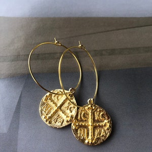 May include: Gold hoop earrings with a round pendant featuring a cross and the text "IC XC NIKA".