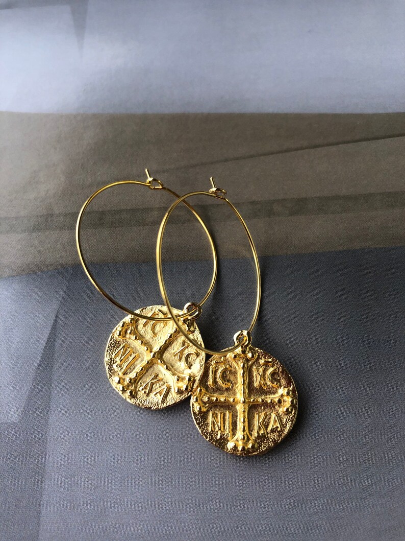 May include: Gold hoop earrings with a round pendant featuring a cross and the text "IC XC NIKA".