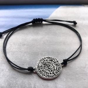 Peut inclure: Bracelet en cordon noir avec un pendentif circulaire argenté orné d'un motif gravé. Le bracelet est réglable grâce à une fermeture coulissante. Les détails complexes du pendentif ajoutent une touche unique à cet accessoire.