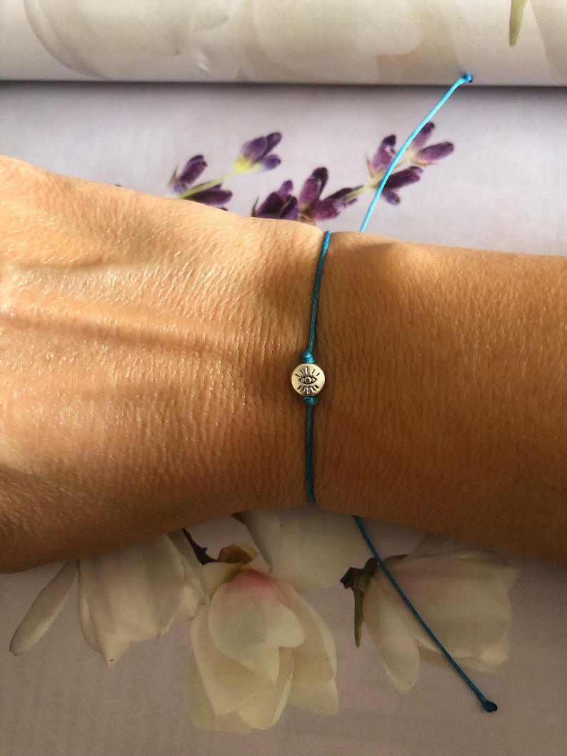 May include: A turquoise blue string bracelet with a silver charm featuring a sun design.