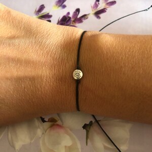 May include: A black string bracelet with a silver charm featuring an eye symbol.