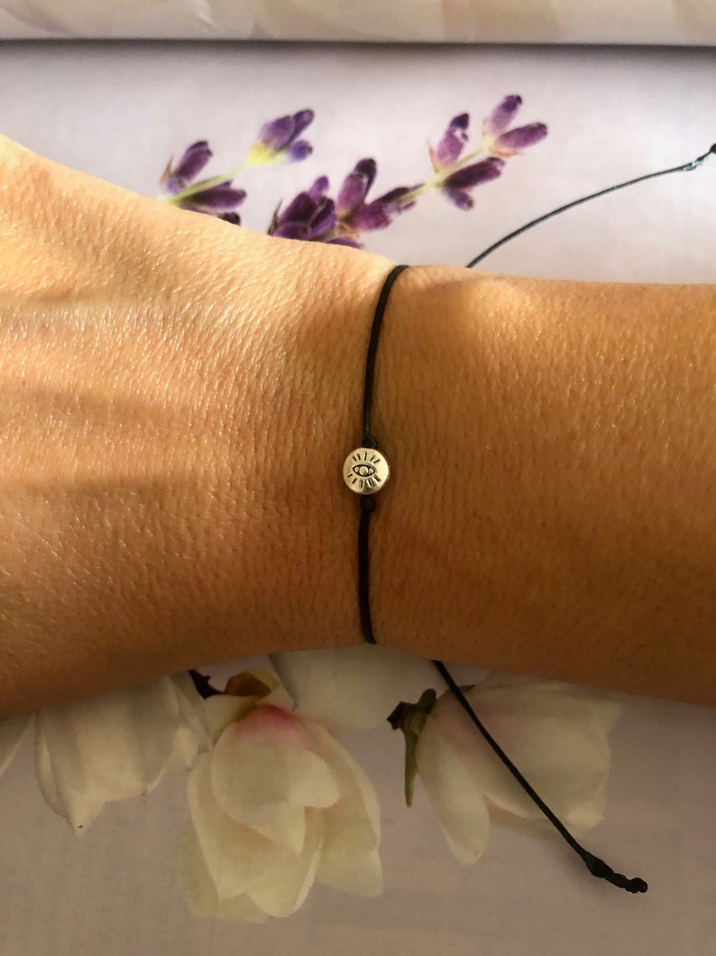 May include: A black string bracelet with a silver charm featuring an eye symbol.