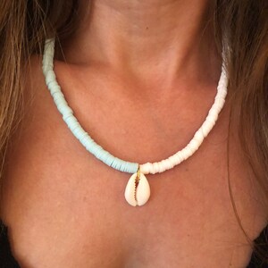 May include: A white and light blue beaded necklace with a small white seashell pendant.