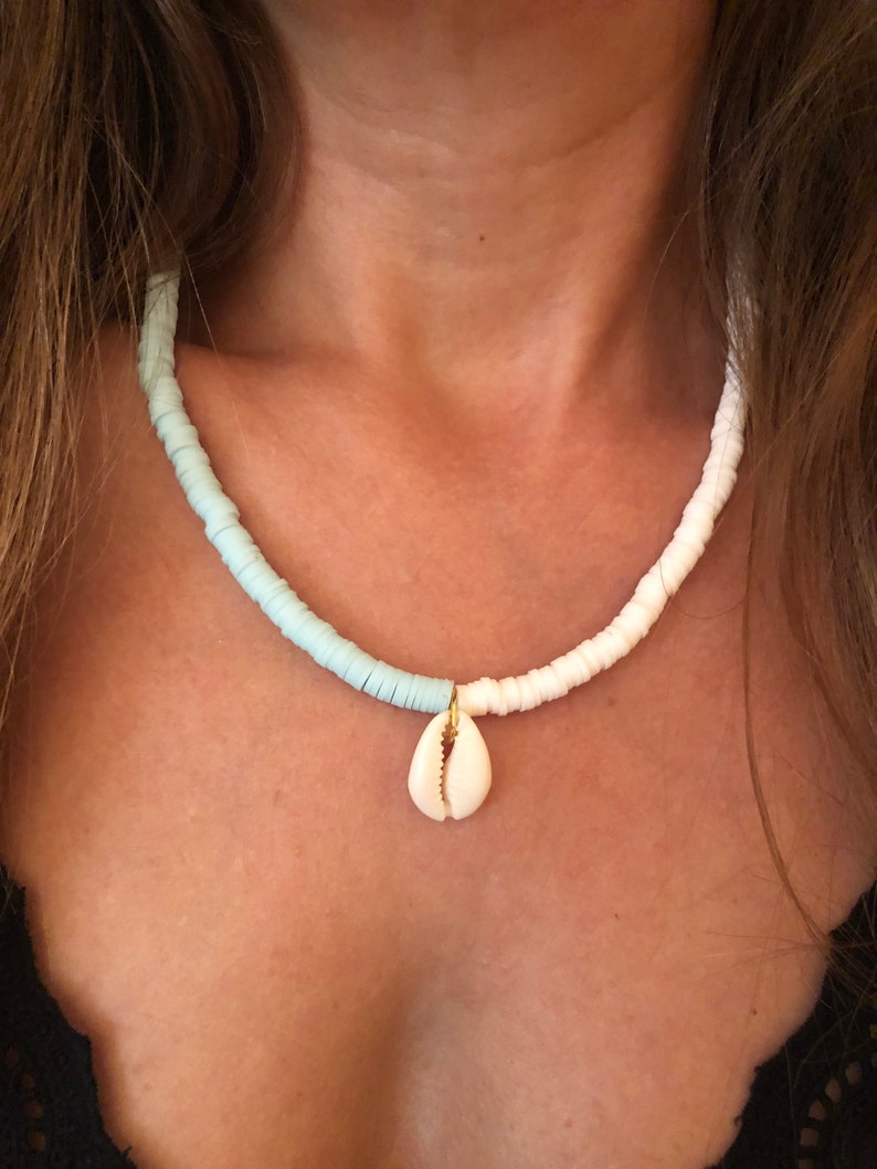 May include: A white and light blue beaded necklace with a small white seashell pendant.