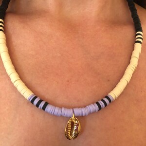 May include: A layered necklace with white, lavender, and black beads, featuring a gold seashell pendant.