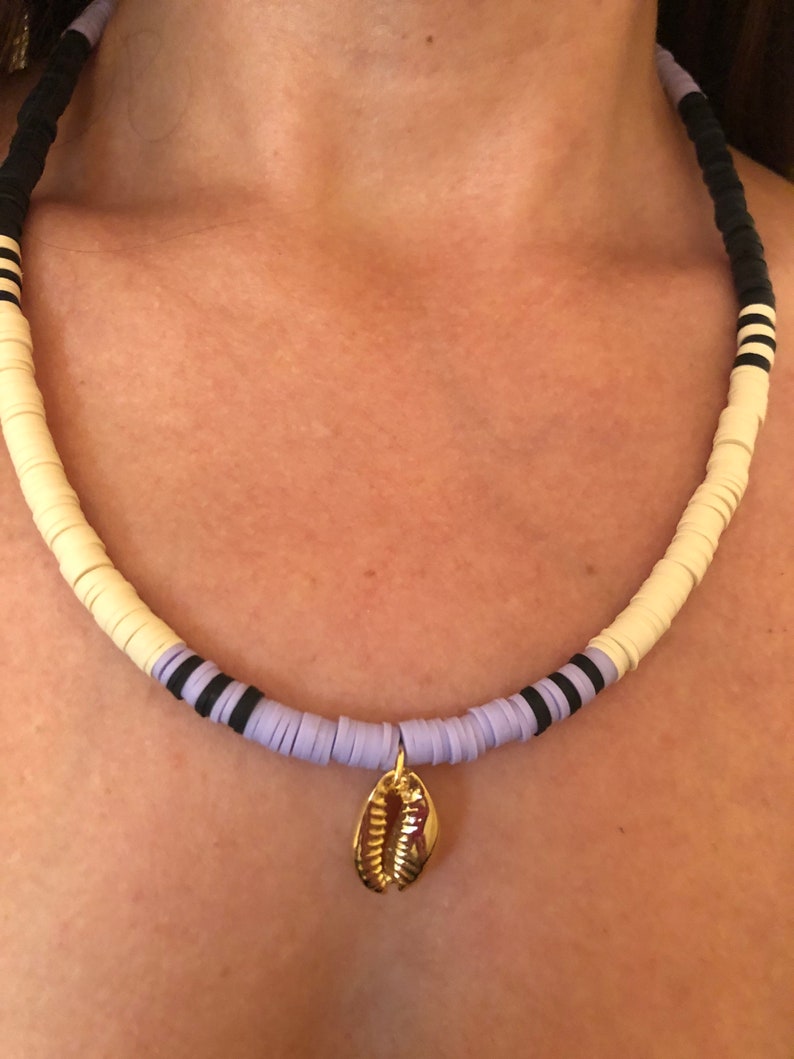 May include: A layered necklace with white, lavender, and black beads, featuring a gold seashell pendant.