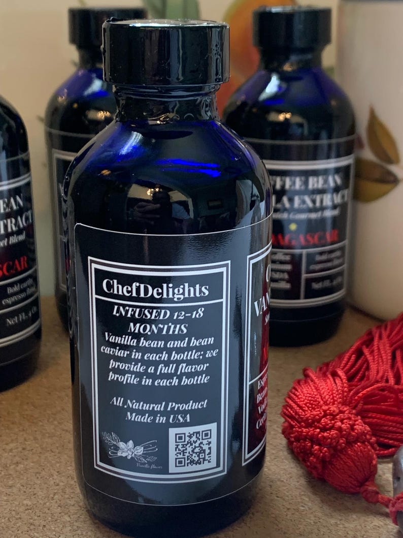 May include: A blue glass bottle with a black label that reads "ChefDelights" and "INFUSED 12-18 MONTHS". The label also includes the text "Vanilla bean and bean caviar in each bottle; we provide a full flavor profile in each bottle". The bottle has a black cap and a QR code on the label. The bottle is sitting on a table with a red tassel.