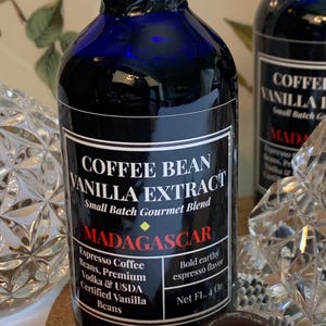 May include: A blue glass bottle with a black label that reads "Coffee Bean Vanilla Extract, Small Batch Gourmet Blend, Madagascar, Espresso Coffee Beans, Premium Vodka & USDA Certified Vanilla Beans, Bold earthy espresso flavor, Net FL. 4 Oz".