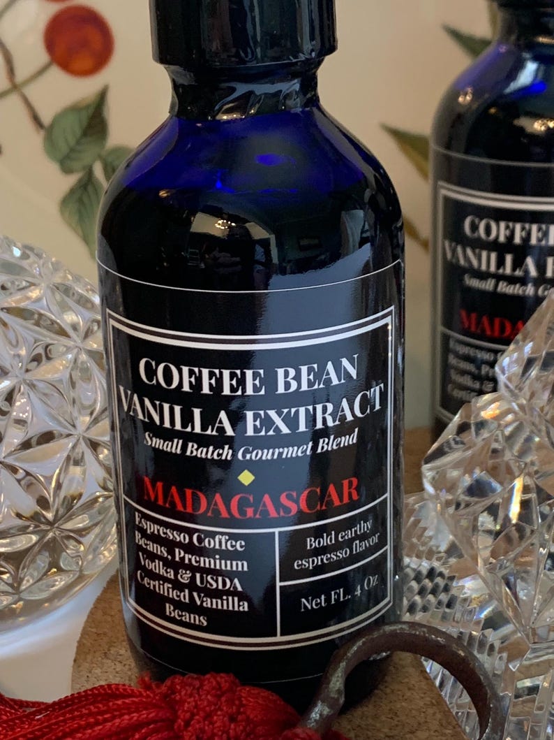 May include: A blue glass bottle with a black label that reads "Coffee Bean Vanilla Extract, Small Batch Gourmet Blend, Madagascar, Espresso Coffee Beans, Premium Vodka & USDA Certified Vanilla Beans, Bold earthy espresso flavor, Net FL. 4 Oz".