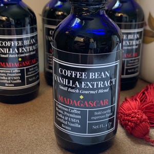 May include: Four small blue glass bottles with black labels containing coffee bean vanilla extract. The label reads "Coffee Bean Vanilla Extract, Small Batch Gourmet Blend, Madagascar, Espresso Coffee Beans, Premium Vodka & USDA Certified Vanilla Beans, Bold Earthy Espresso Flavor, Net FL. 4 Oz."