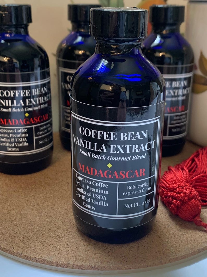 May include: Four small blue glass bottles with black labels containing coffee bean vanilla extract. The label reads "Coffee Bean Vanilla Extract, Small Batch Gourmet Blend, Madagascar, Espresso Coffee Beans, Premium Vodka & USDA Certified Vanilla Beans, Bold Earthy Espresso Flavor, Net FL. 4 Oz."
