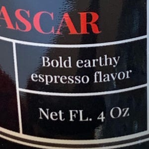 May include: Black and white label with red text that reads "ASCAR" and the words "Bold earthy espresso flavor" and "Net FL. 4 Oz".