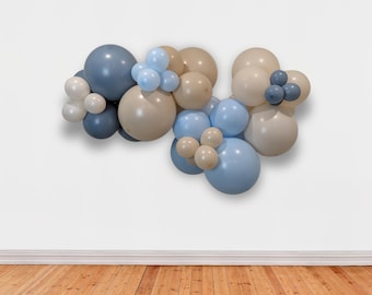 Könnte beinhalten: Eine Ballon-Girlande mit blauen, beigen und weißen Ballons. Die Girlande ist in einer kaskadierenden Anordnung angeordnet, wobei die Ballons unterschiedliche Größen haben.