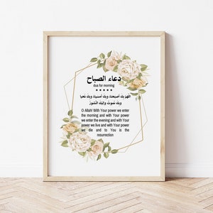Puede incluir: Impresión enmarcada con caligrafía árabe y traducción al inglés. La obra de arte presenta acentos florales crema y melocotón alrededor de una forma geométrica. El texto dice "Dua for Morning" y una oración.