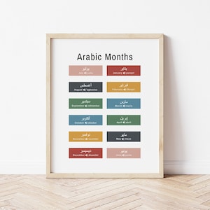 May include: A framed print titled "Arabic Months" displays the English and Arabic names for each month. The design features a white background with colourful rectangular blocks for each month, and a light wooden frame.