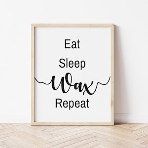 May include: A framed print with the words "Eat Sleep Wax Repeat" in black script and block letters. The print has a white background and a light wood frame, suitable for a salon or spa.